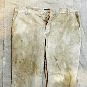 May include: A pair of light brown trousers with a tie at the waist. The trousers have a faded, distressed look with brown stains.
