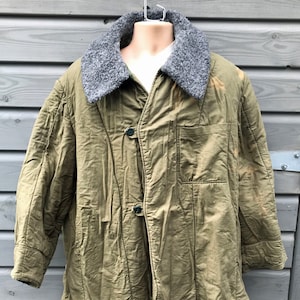 May include: An olive green quilted jacket with a gray faux fur collar. The jacket has a button-up front, a chest pocket, and long sleeves. The jacket is displayed on a mannequin.