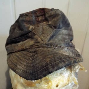 May include: A dark gray, worn, cotton cap with a slightly curved brim. The cap has a faded, distressed look and appears to be vintage.