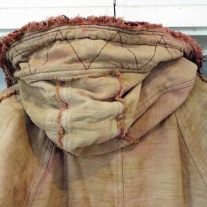 May include: A tan hooded jacket with a frayed edge and a red-brown dye. The hood has a diamond-shaped stitching pattern.