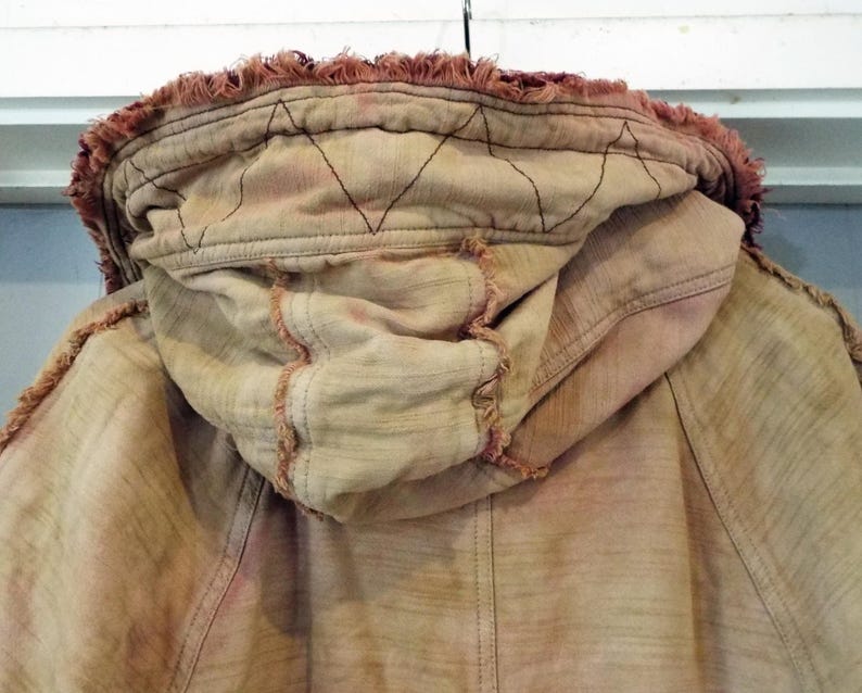 May include: A tan hooded jacket with a frayed edge and a red-brown dye. The hood has a diamond-shaped stitching pattern.