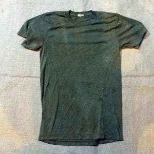 Puede incluir: Una camiseta verde oscuro con un aspecto descolorido. La camiseta tiene mangas cortas y cuello redondo.