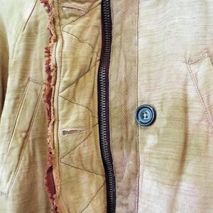 May include: Close-up of a beige jacket with a zipper and a button closure. The jacket has a quilted lining and a frayed edge detail.