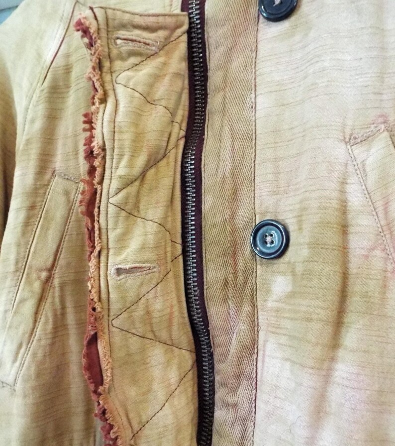 May include: Close-up of a beige jacket with a zipper and a button closure. The jacket has a quilted lining and a frayed edge detail.