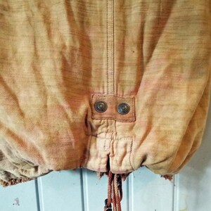 May include: A tan colored jacket with a drawstring at the bottom and two metal buttons on the back.
