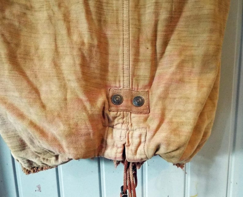 May include: A tan colored jacket with a drawstring at the bottom and two metal buttons on the back.