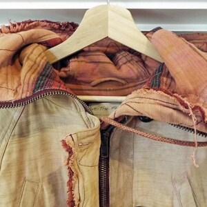 May include: A tan jacket with a red and brown patterned hood. The jacket has a zipper closure and a drawstring hood.