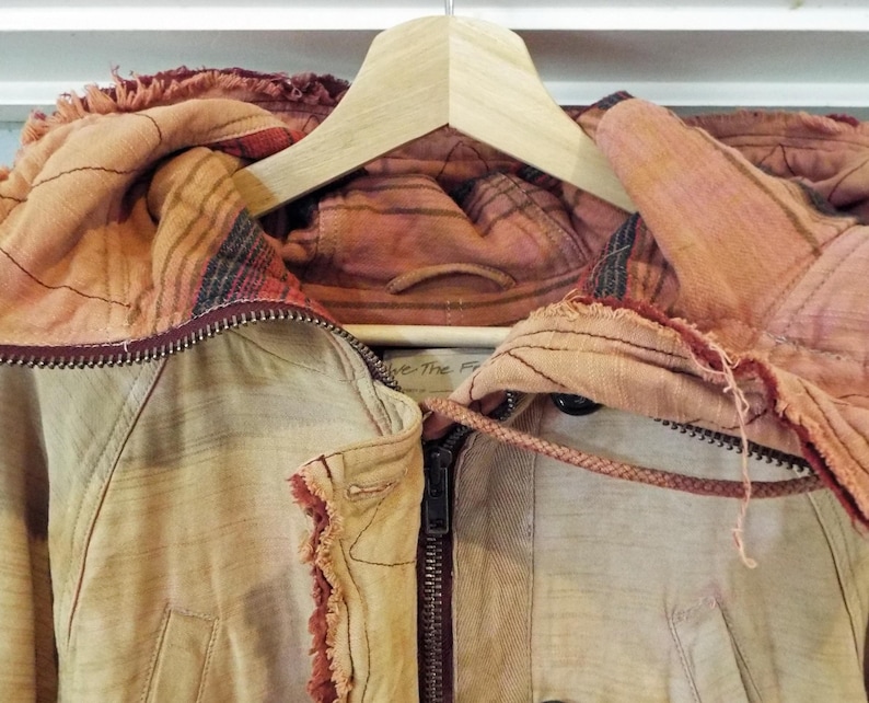 May include: A tan jacket with a red and brown patterned hood. The jacket has a zipper closure and a drawstring hood.