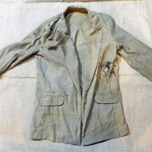 May include: A light green blazer with a few dark brown stains and a small hole on the right side of the jacket.