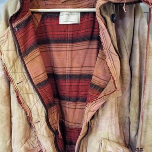 May include: A cream-colored jacket with a red and black plaid lining. The jacket has a zipper closure and a hood. The label on the jacket reads "We The Free".