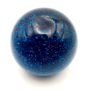May include: A round, dark blue object with a shiny surface. It's covered in small, glittering blue specks, giving it a starry appearance. The object is placed on a simple white background, which emphasizes its colour and texture.