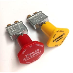 May include: Two air brake control valves. One is red and labeled "TRAILER AIR SUPPLY" and "EVACUATE". The other is yellow and labeled "PARKING BRAKE". Both have silver metal housings with text that reads "75 AMPS".