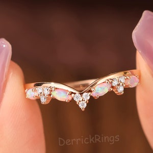 Può includere: Un delicato anello in oro rosa con un design a forma di V. L'anello è adornato con piccole pietre di zircone cubico trasparenti e pietre di opale ovali.