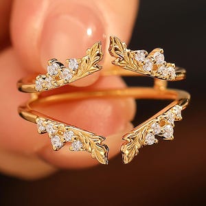 Pu&ograve; includere: Un anello color oro dal design unico. L'anello presenta quattro elementi decorativi a forma di foglia, ciascuno ornato da piccole pietre bianche scintillanti. Il design dell'anello &egrave; intricato ed elegante, adatto alle occasioni speciali.