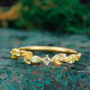 May include: A delicate gold band ring with a leafy design and pear-shaped green gemstones. The ring is set with small, clear diamonds.