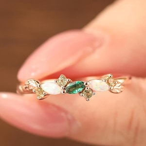 May include: A delicate gold ring with a cluster of white and green gemstones. The ring features a marquise-shaped green stone surrounded by smaller white and yellow stones.