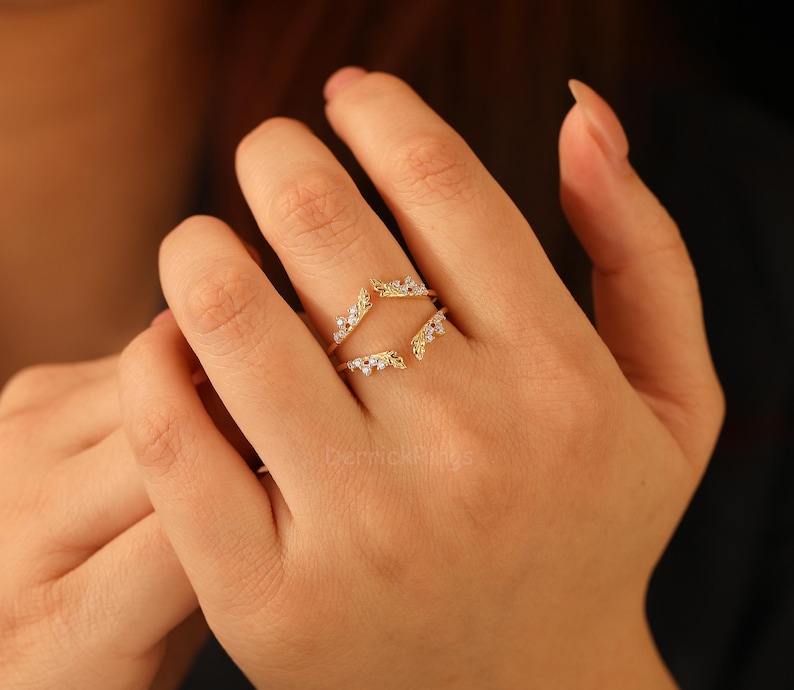 Pu&ograve; includere: Un anello dorato con piccole pietre preziose trasparenti. L'anello ha un design unico, con due fasce curve che si incontrano nella parte superiore e inferiore. Le pietre preziose sono incastonate in un motivo delicato, aggiungendo brillantezza.