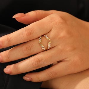 Pu&ograve; includere: Un anello dorato dal design unico, con piccole pietre scintillanti. L'anello ha uno stile aperto e avvolgente con dettagli decorativi a forma di foglie. L'anello &egrave; mostrato su una mano con unghie curate.