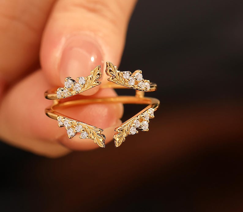 Pu&ograve; includere: Un anello color oro dal design unico. L'anello presenta quattro elementi decorativi a forma di foglia, ciascuno ornato da piccole pietre bianche scintillanti. Il design dell'anello &egrave; intricato ed elegante, adatto alle occasioni speciali.