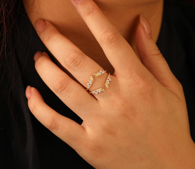 Pu&ograve; includere: Un anello color oro dal design unico. L'anello presenta una doppia fascia con una forma geometrica al centro, ornata da piccole pietre scintillanti. L'anello &egrave; progettato per essere indossato attorno a un anello esistente.