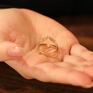 Pu&ograve; includere: Un anello dorato con un design aperto unico, tenuto in una mano. L'anello presenta una doppia fascia e elementi decorativi alle estremit&agrave; aperte. L'anello &egrave; probabilmente realizzato in metallo dorato ed &egrave; progettato per essere indossato come accessorio di moda.