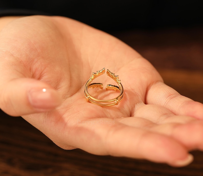 Pu&ograve; includere: Un anello dorato con un design aperto unico, tenuto in una mano. L'anello presenta una doppia fascia e elementi decorativi alle estremit&agrave; aperte. L'anello &egrave; probabilmente realizzato in metallo dorato ed &egrave; progettato per essere indossato come accessorio di moda.