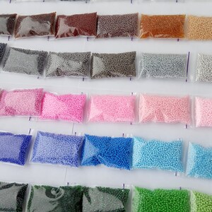 May include: Assortment of small, colorful beads in clear plastic bags. The beads are in various shades, including brown, gray, pink, blue, and green. The bags are arranged in neat rows, suggesting a craft supply or DIY project.