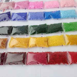 May include: A collection of small, colorful beads in clear plastic bags, arranged in rows. The beads are in various shades, including pink, blue, green, yellow, and red. The image suggests a craft or DIY project, possibly for jewelry making or embroidery.