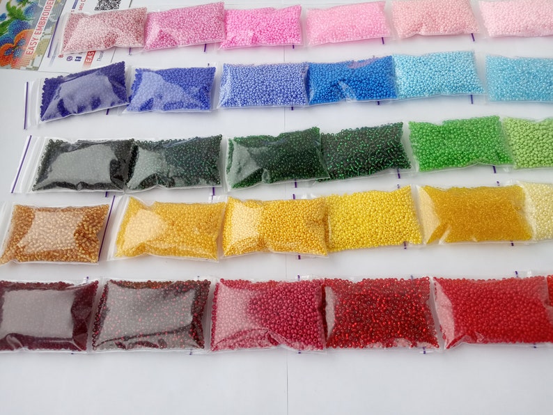 May include: A collection of small, colorful beads in clear plastic bags, arranged in rows. The beads are in various shades, including pink, blue, green, yellow, and red. The image suggests a craft or DIY project, possibly for jewelry making or embroidery.