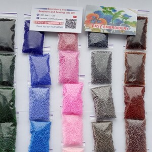May include: A collection of small, colorful beads in clear plastic bags. The beads are in various colors, including red, yellow, green, blue, pink, gray, brown, white, and purple. The bags are arranged in rows, with a card that reads "EASY EMBROIDERY".