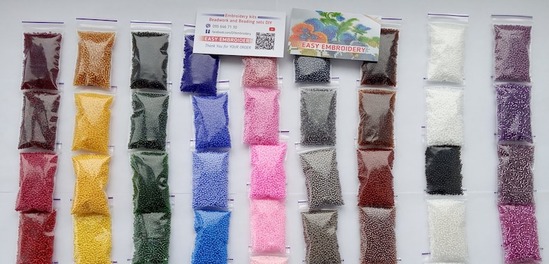 May include: A collection of small, colorful beads in clear plastic bags. The beads are in various colors, including red, yellow, green, blue, pink, gray, brown, white, and purple. The bags are arranged in rows, with a card that reads "EASY EMBROIDERY".