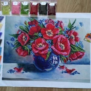 以下が含まれることがあります： 青い花瓶に赤いポピーの花束が描かれたダイヤモンドペイントキットのアップ。キットにはキャンバス、ビーズ、説明書が含まれています。パッケージのテキストは「Червоні тюльпани DANA-3189 EASY EMBROIDERY」です。