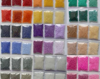 May include: Assortment of small, round seed beads in various colours, packaged in individual clear plastic bags. The colours include red, orange, yellow, green, blue, purple, pink, white, silver, and grey.