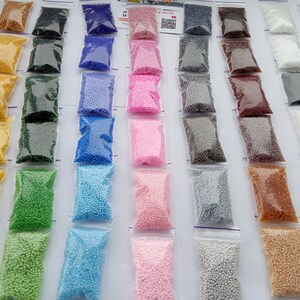 May include: Assortment of small, colorful beads in clear plastic zip-top bags. The beads are in various colors, including yellow, green, blue, pink, and brown. The bags are arranged in neat rows, creating a visually appealing display.