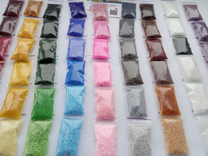 May include: Assortment of small, colorful beads in clear plastic zip-top bags. The beads are in various colors, including yellow, green, blue, pink, and brown. The bags are arranged in neat rows, creating a visually appealing display.