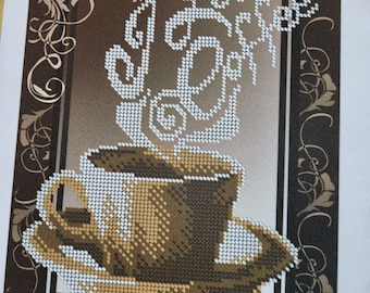 Op de afbeelding: Een bruin en wit kruissteekontwerp van een kopje koffie met stoom die eruit opstijgt. Het ontwerp is omlijst met een bruine en gouden sierlijke rand.