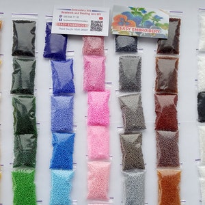 May include: A collection of small, colorful beads in clear plastic bags, arranged in vertical rows. The beads come in various colors, including red, yellow, green, blue, pink, and purple. The image also includes a small card with the text "EASY EMBROIDERY".
