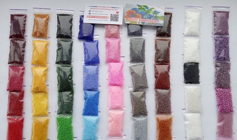 May include: A collection of small, colorful beads in clear plastic bags, arranged in vertical rows. The beads come in various colors, including red, yellow, green, blue, pink, and purple. The image also includes a small card with the text "EASY EMBROIDERY".