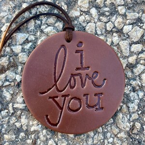 May include: A brown leather ornament with a cord for hanging. The ornament has the words "I love you" embossed on the front.