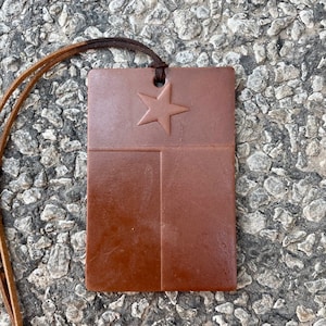 May include: A brown leather keychain with a cutout of the Texas flag. The flag features a white star on a blue background with a red stripe at the bottom.