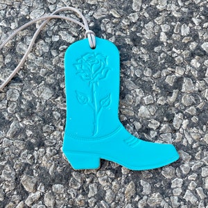 May include: A turquoise blue boot-shaped ornament with a raised floral design. The ornament has a white cord attached to the top.