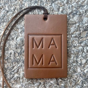 May include: A brown leather tag with a string attached. The tag has the word "MAMA" embossed in a square.
