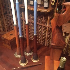 May include: Four wooden candle holders with white and blue candles. The holders have a dark brown finish with brass accents and decorative bases. A wooden box and a wine bottle are also visible.
