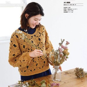 May include: A crocheted sweater in a mustard yellow color with a lacy pattern. The sweater has a round neckline and long sleeves. The sweater is shown on a model with a dark blue shirt underneath.