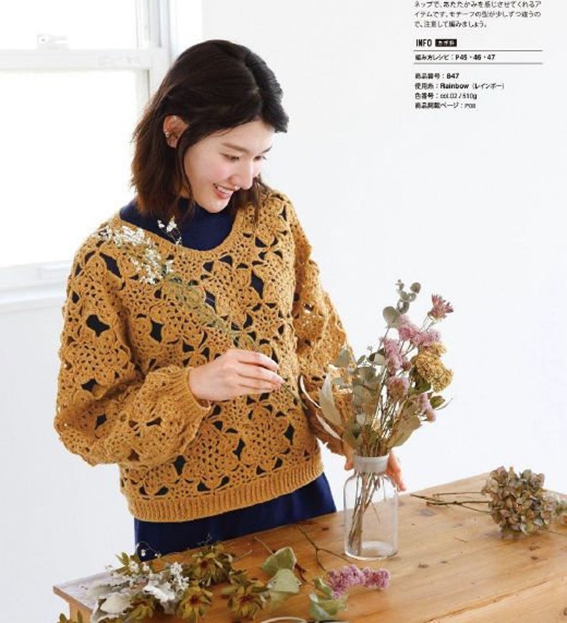 May include: A crocheted sweater in a mustard yellow color with a lacy pattern. The sweater has a round neckline and long sleeves. The sweater is shown on a model with a dark blue shirt underneath.