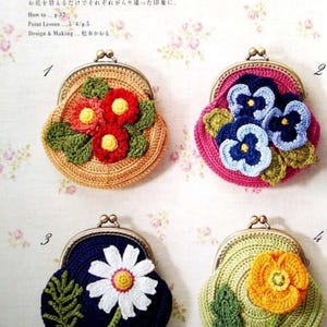 Op de afbeelding: Vier gehaakte portemonnees met verschillende bloemenontwerpen. De portemonnees zijn beige, roze, donkerblauw en groen. Elke portemonnee heeft een metalen sluiting.