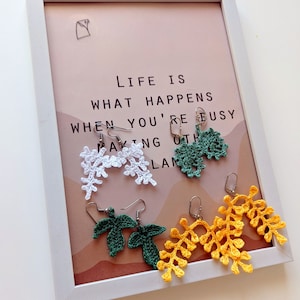 May include: Four pairs of crocheted earrings in the shape of leaves. Two pairs are green, one pair is white, and one pair is yellow.