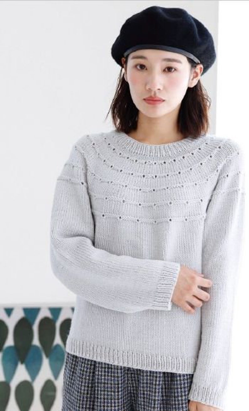May include: A light gray knitted sweater with a delicate openwork pattern around the neckline. The sweater has long sleeves and a relaxed fit.