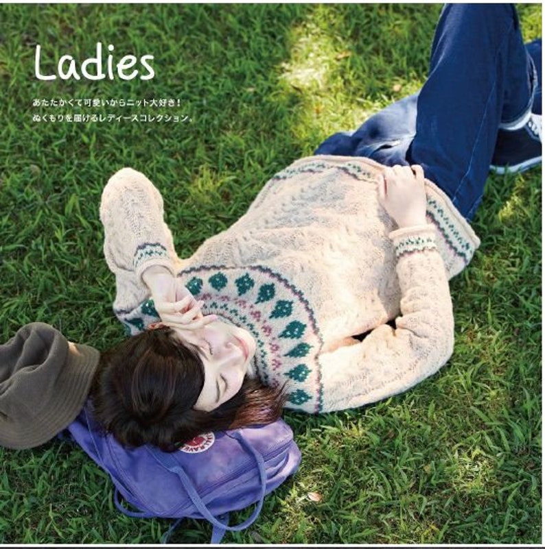 May include: A woman wearing a light beige sweater with a green, pink, and white patterned design. The sweater has a cable knit texture. The woman is lying on her back on a bed of green grass. The text "Ladies" is visible in the top left corner of the image. The text "あったかくって可愛いからニット大好き！" and "あたらしい風合いが楽しめるアーミーコレクション." is visible in the top left corner of the image.