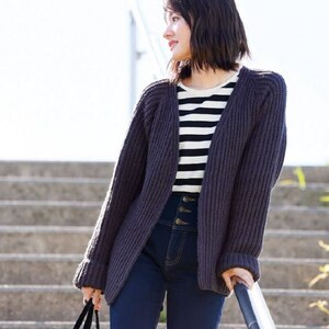 May include: A woman wearing a dark gray knitted cardigan with a striped shirt underneath and dark blue jeans. She is standing on a set of stairs and holding onto a railing.